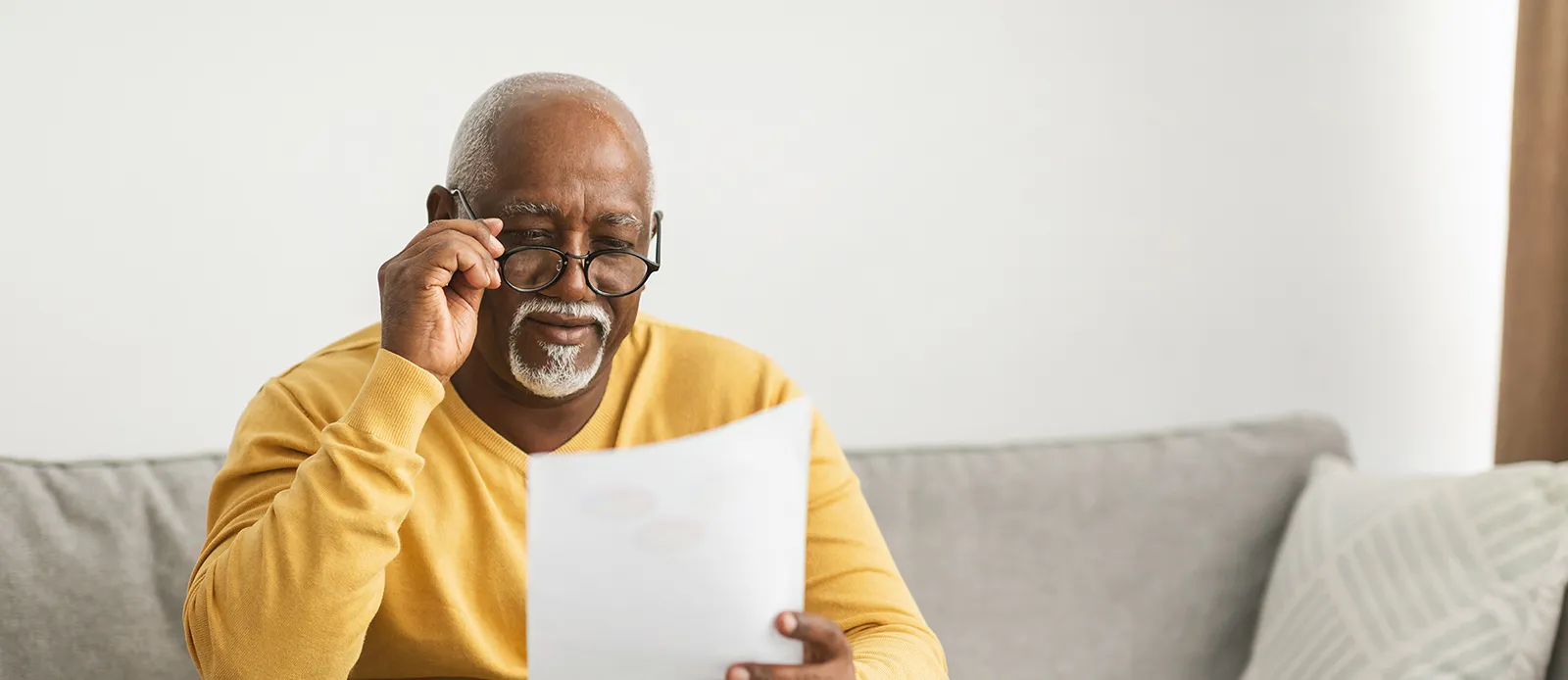 Senior African American Male Working With Papers Wearing Eyeglasses Sitting On Couch At Home.
